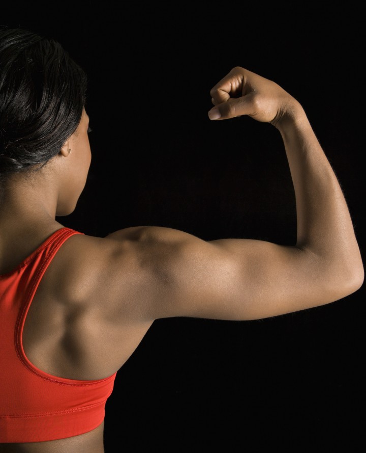 Back view of African American woman flexing muscular bicep.