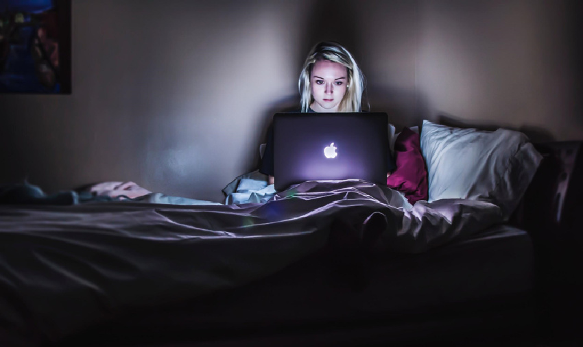Woman sitting on a bed with an open laptop.