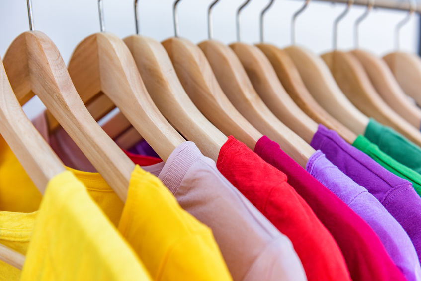 Fashion clothes hanging on clothing rack - bright colorful selection of clothes closet. Rainbow color choice of trendy girl outfits on hangers 