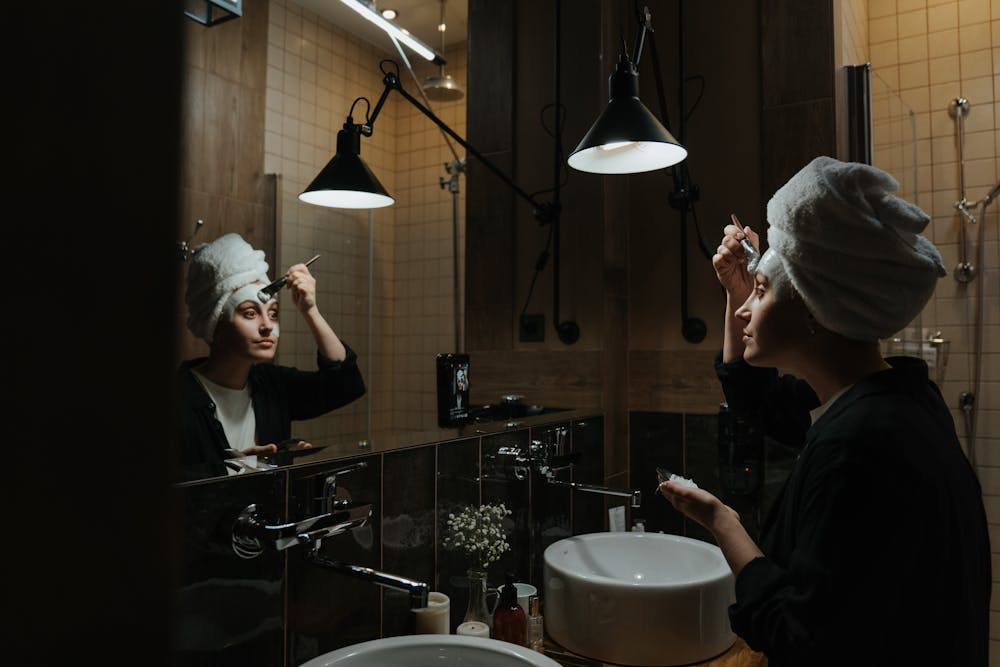 A woman applying skincare in a bathroom mirror reflection