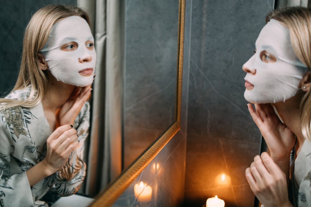 A woman with a sheet mask looking at the mirror.