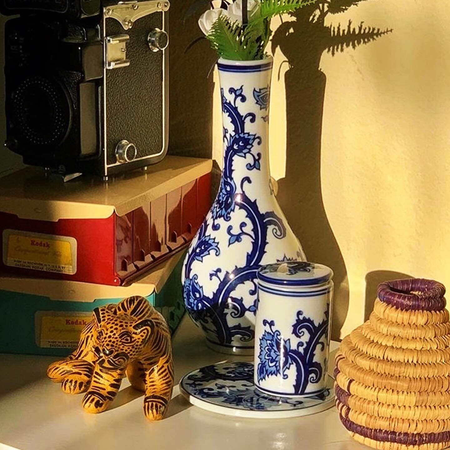The My Bud Vase Joy porcelain vase bong styled on a shelf with faux botanicals, positioned naturally alongside a vintage Kodak camera, woven basket, and tiger figurine.