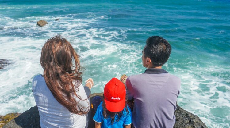 family sitting on a rock at ocean