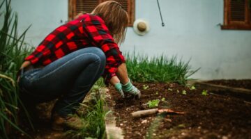 Woman tending plants in an outdoor garden, wearing casual attire and gloves